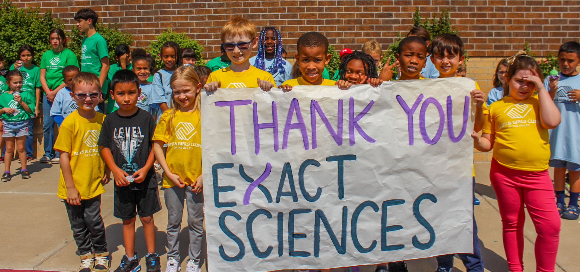 Kids posing with sign reading "Thank you Exact Sciences"