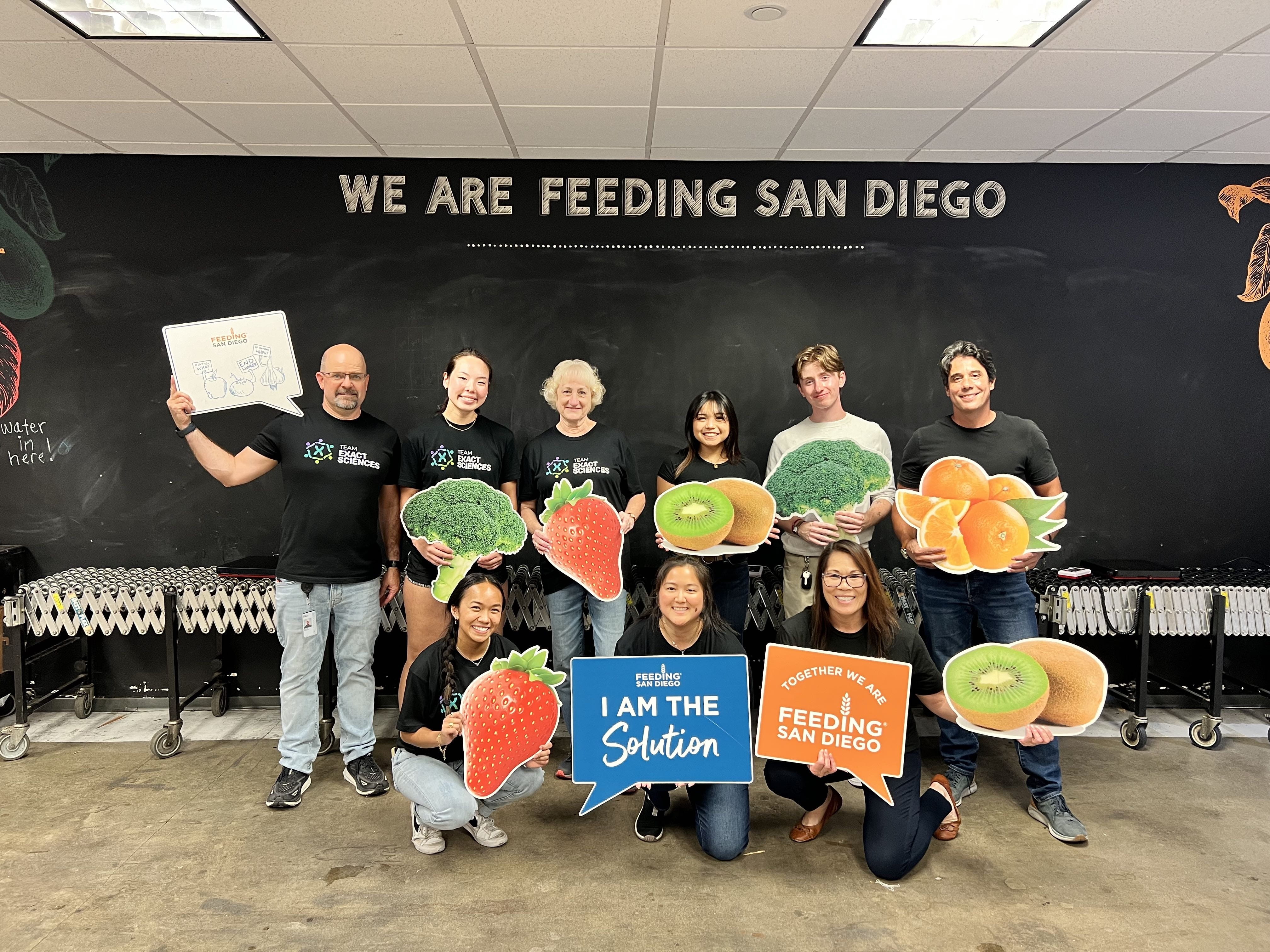 A group of volunteers holding signs featuring various fruits, vegetables and supportive words after volunteering.