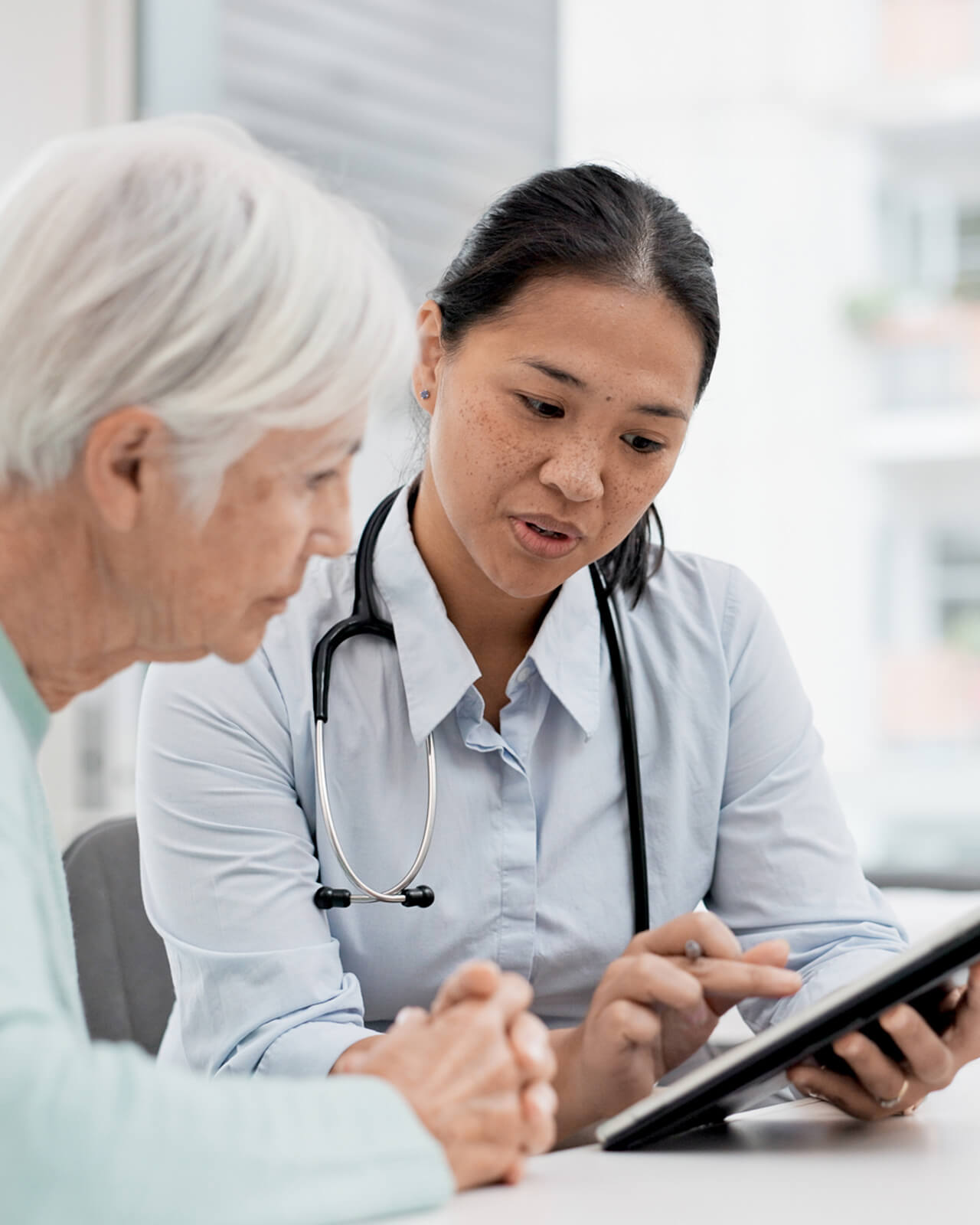 A health care provider with stethoscope looking at a tablet device with a patient.