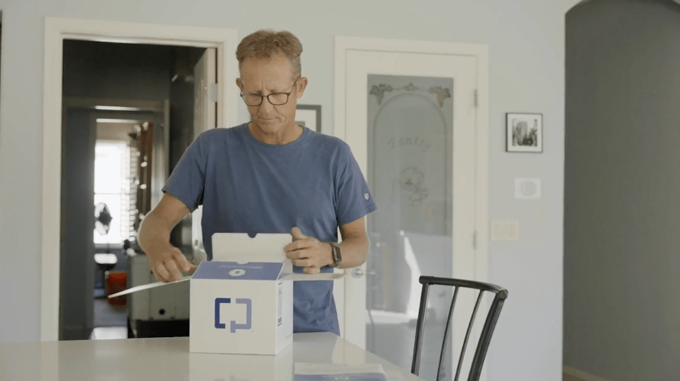 A patient opening a Cologuard box at a dining table